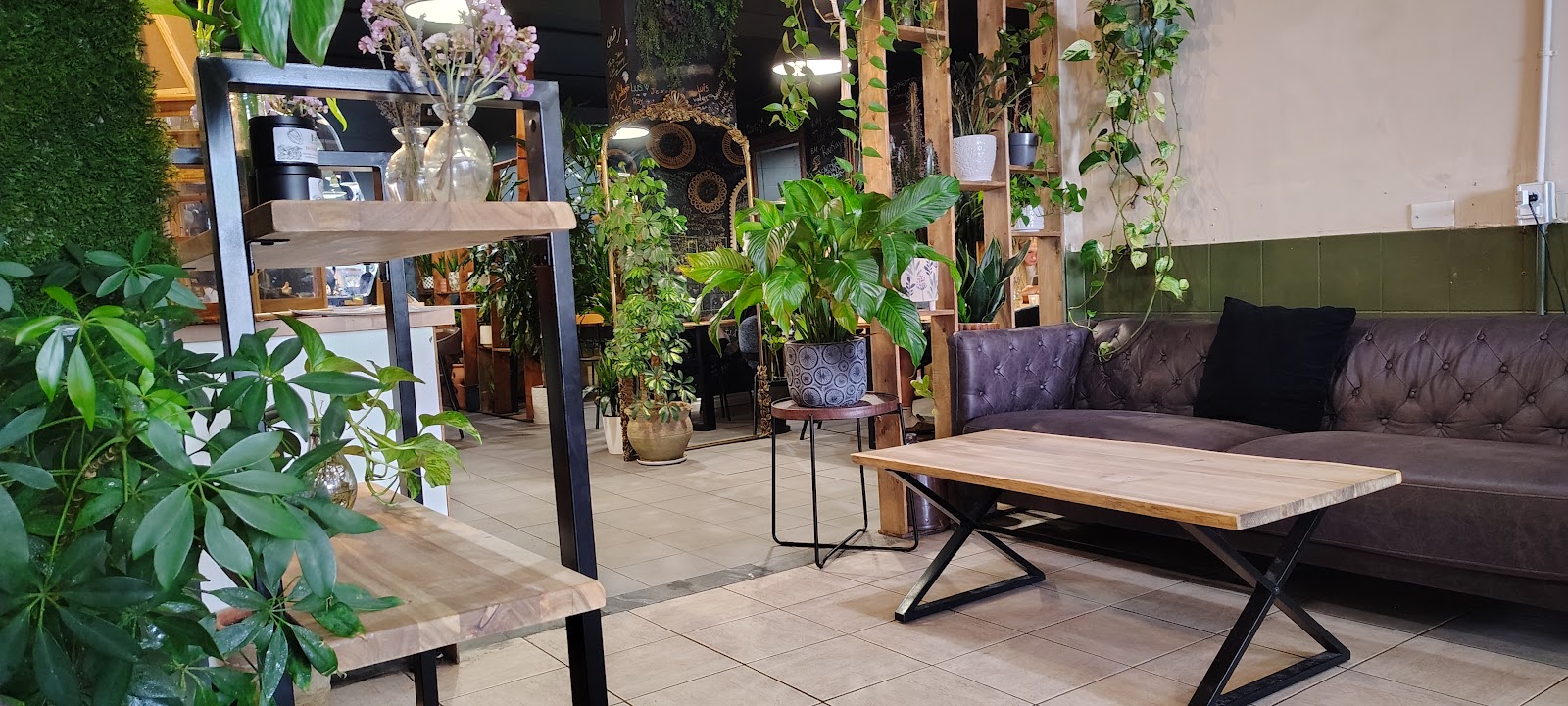 Coin salon du Café T&M, canapé en cuir capitonné, table en bois et plantes